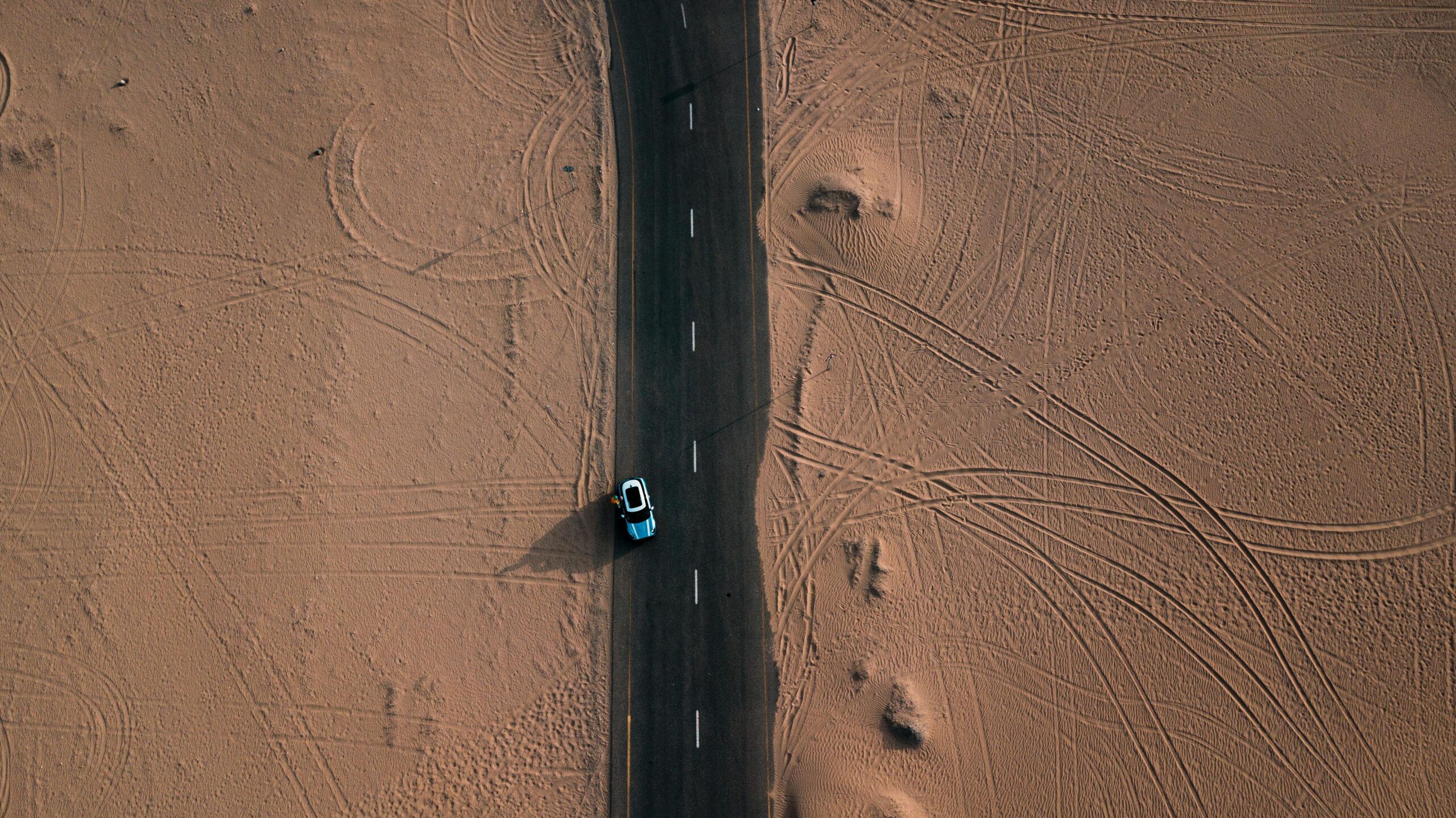 Drone view of a car driving through a desert road in Dubai, UAE.mashaer fleet
